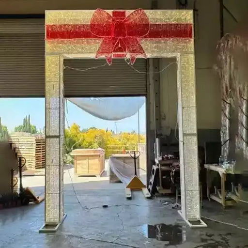 14FT Gold Gift Box Walkthrough Arch decorated with warm white lights and illuminated red bow