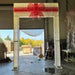 14FT Gold Gift Box Walkthrough Arch decorated with warm white lights and illuminated red bow